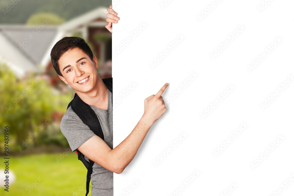 Teenage boy with backpack pointing on blank white sign