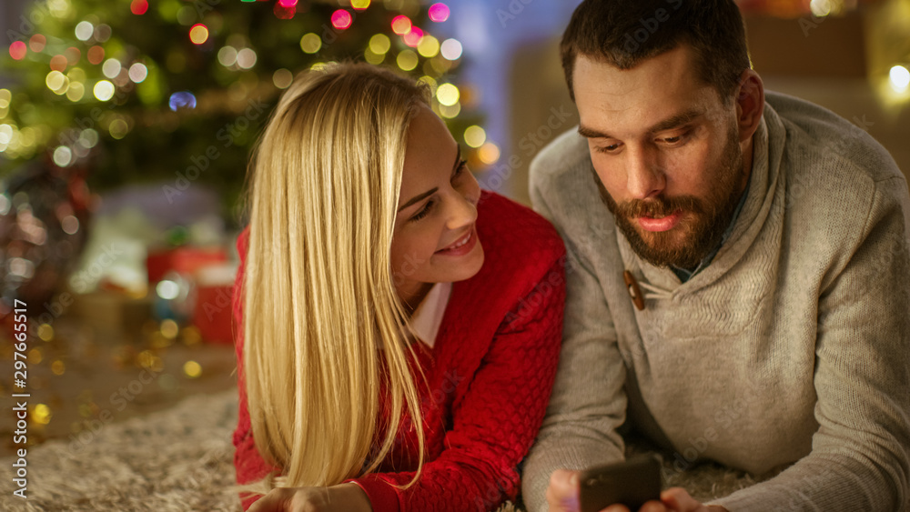 Happy Lovely Couple Lies On the Carpet Under Christmas Tree, They Look at Something Interesting on t