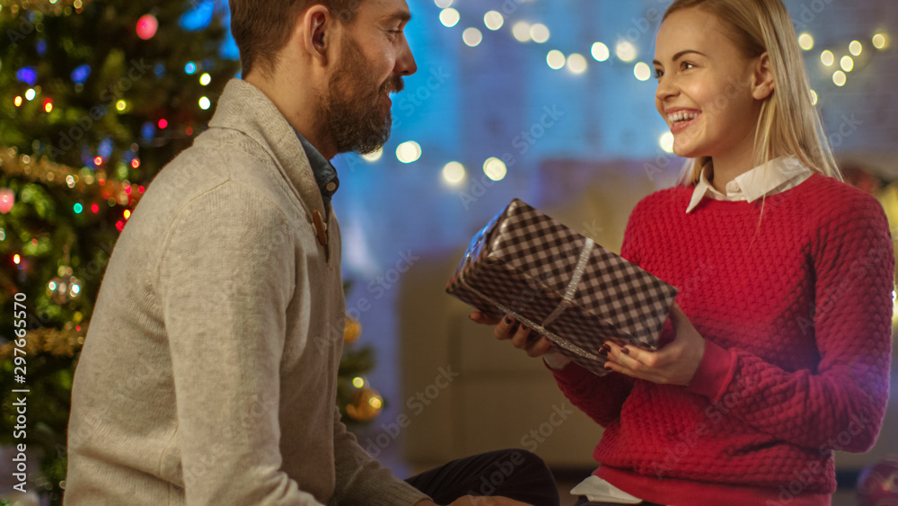 英俊的男人给他漂亮的女友送圣诞礼物。他们和Decora在一个明亮的房间里