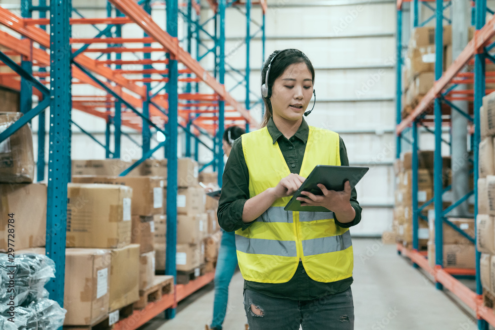 Businesswoman using digital tablet in distribution warehouse. young woman staff in headset talking t