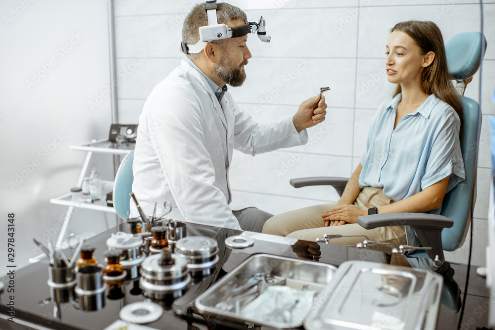 Senior otolaryngologist preparing for the medical examination procedure for a woman patient in the m