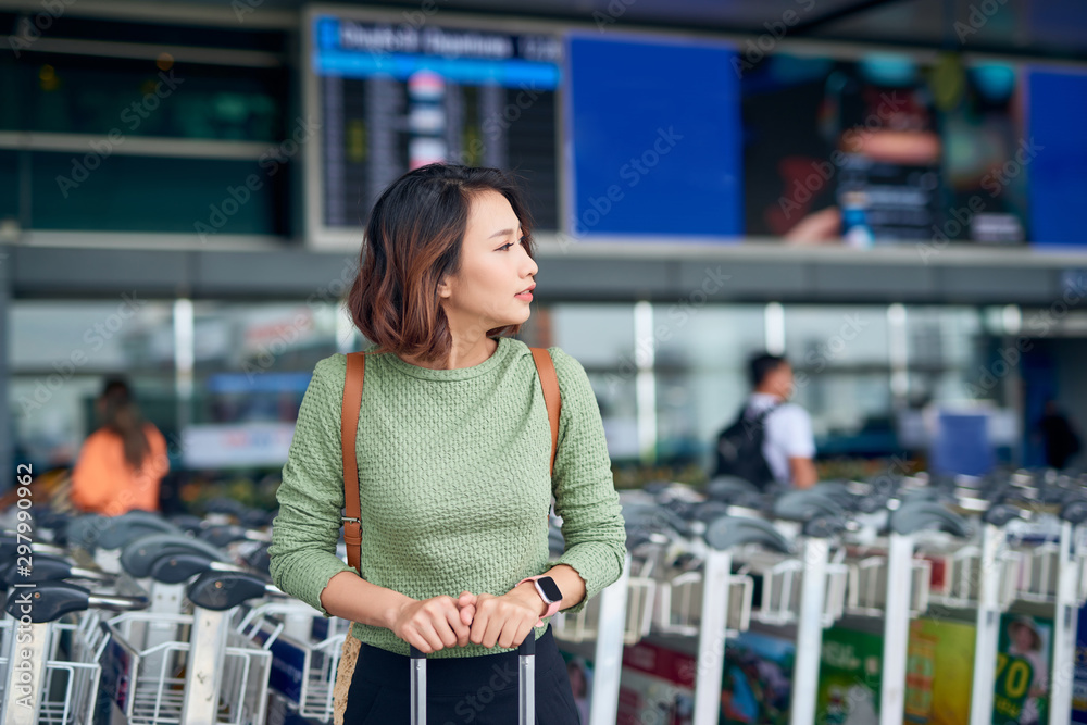 亚洲年轻女子提着行李箱站在机场等公交车。