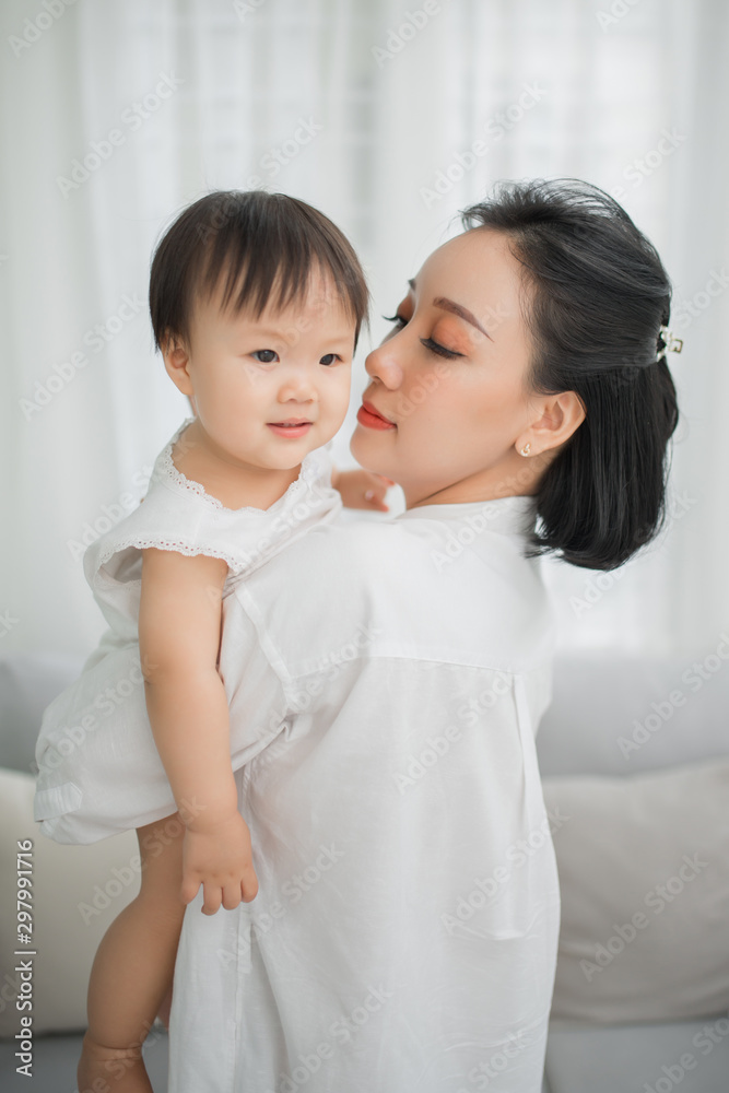 Mother hugging and kissing her little girl in living room, Kid at home.