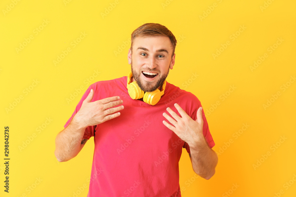 Surprised young man with headphones on color background