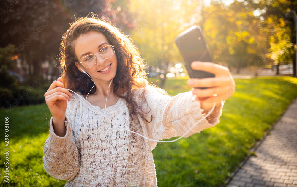 Portrait of a pretty smiling young woman using mobile phone while walking on city street