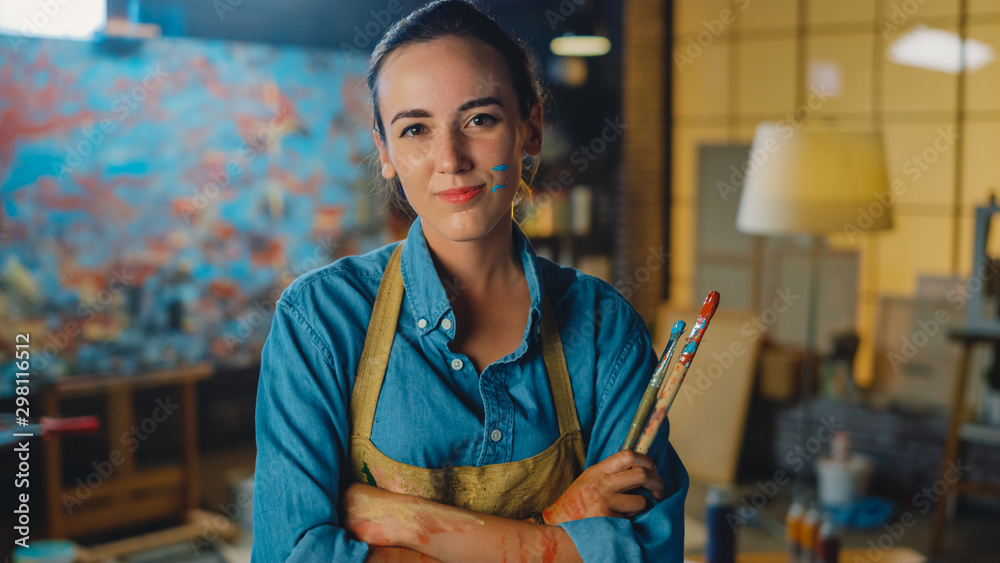 Young Female Artist Dirty with Paint, Wearing Apron, Crosses Arms while Holding Brushes, Looks at th