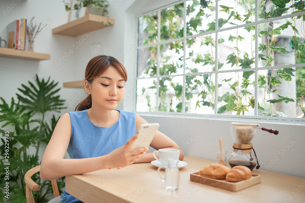 Asian woman using phone while having breakfast