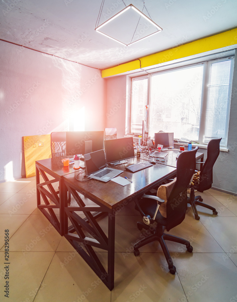 Chairs at wooden modern table with laptops .Wide window and yellow emphasis above it. Bright sticker