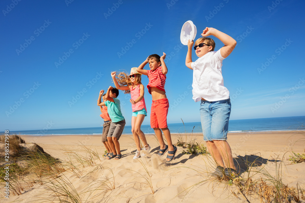 Many kids jump on the beach near sea lifting hands