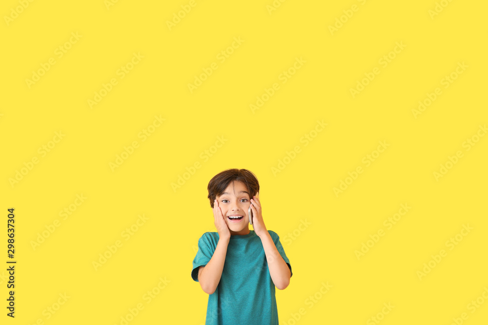 Surprised little boy talking by mobile phone on color background