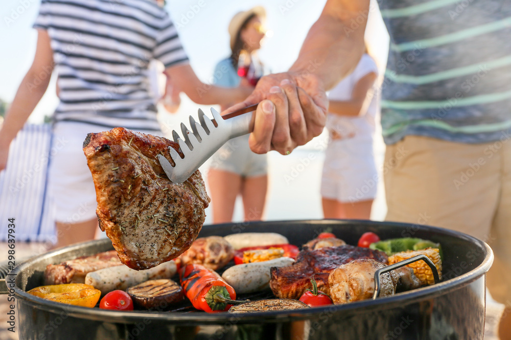 Man cooking tasty meat on barbecue grill outdoors, closeup