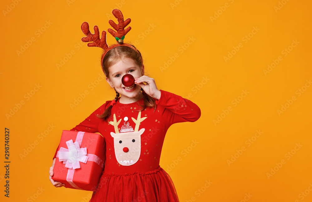 happy funny child girl in red Christmas reindeer costume with gift on yellow   background.