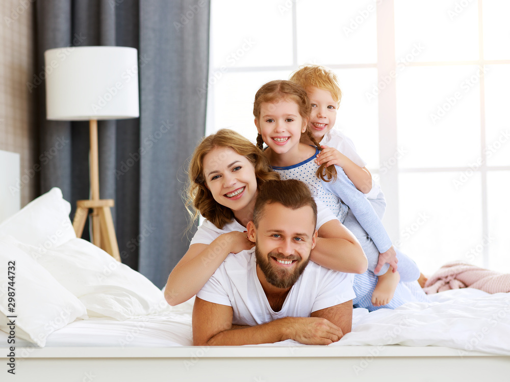  happy family mother, father and children laughing, playing and smiling in bed   at home.