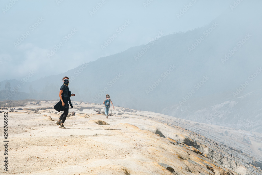 戴着防护口罩的年轻女性在卡瓦伊詹火山口周围的荒地上行走。后世界末日