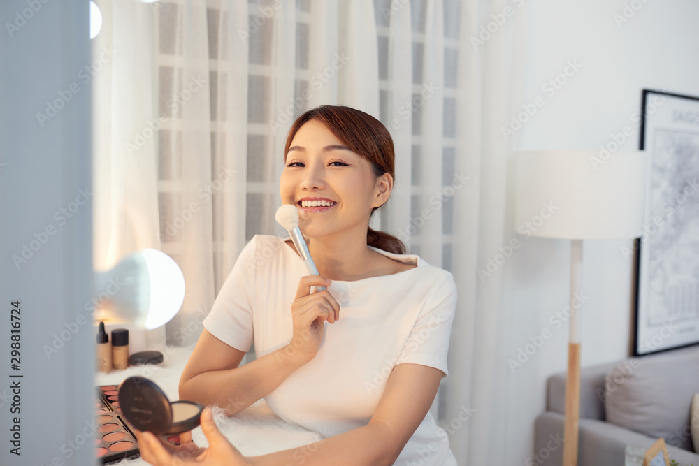 Happy young Asian woman applying makeup on face with big brush