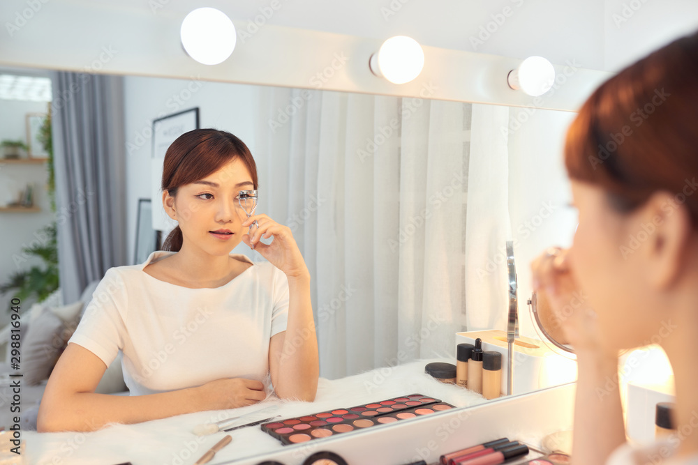 Portrait of beautiful young Asian woman looking at the mirror using eyelash curler