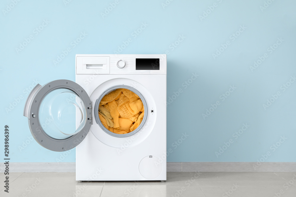 Modern washing machine with laundry near color wall