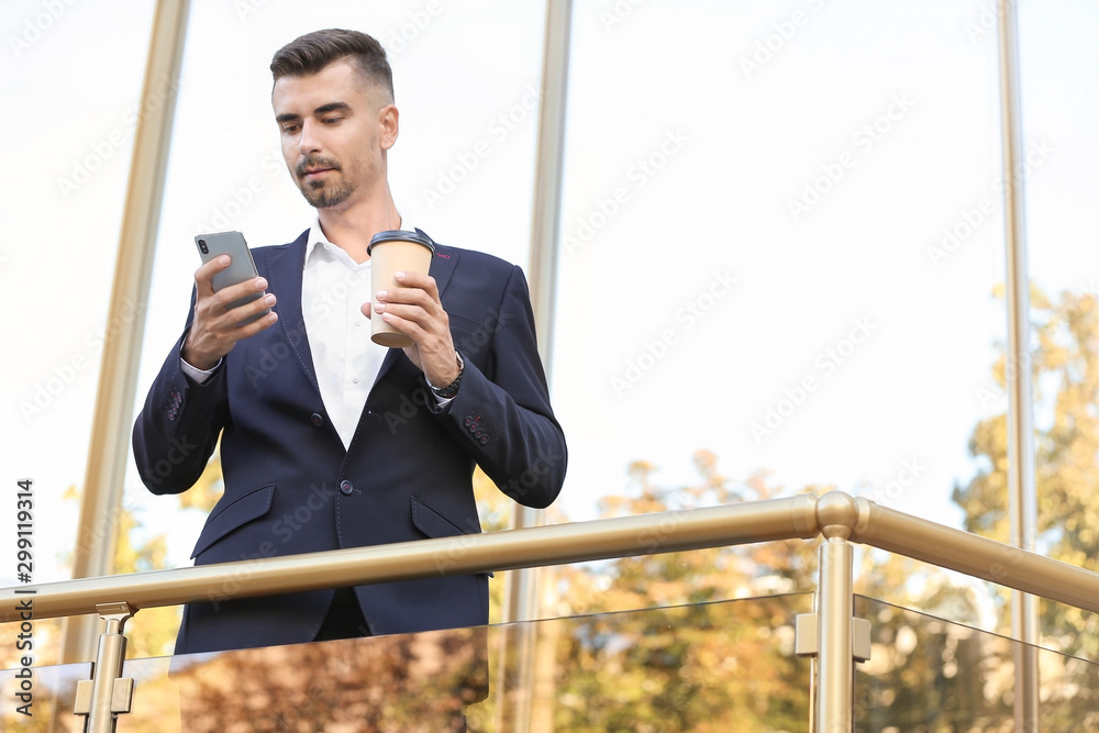 一位英俊的商人在户外拿着一杯咖啡和手机的肖像