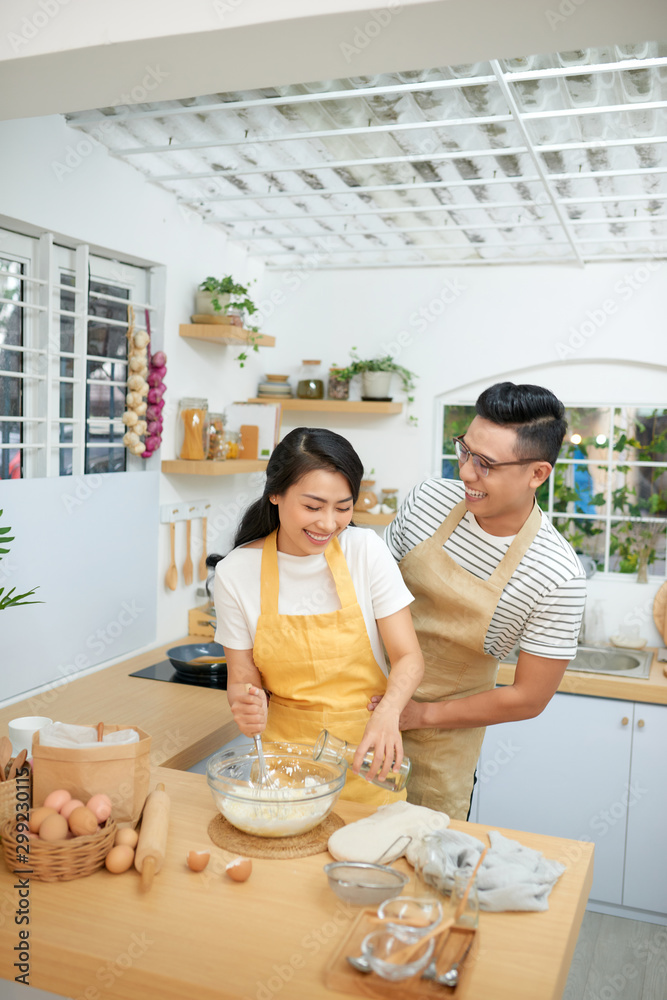 Couple man and woman wearing aprons having fun while making homemade pasta in kitchen at home