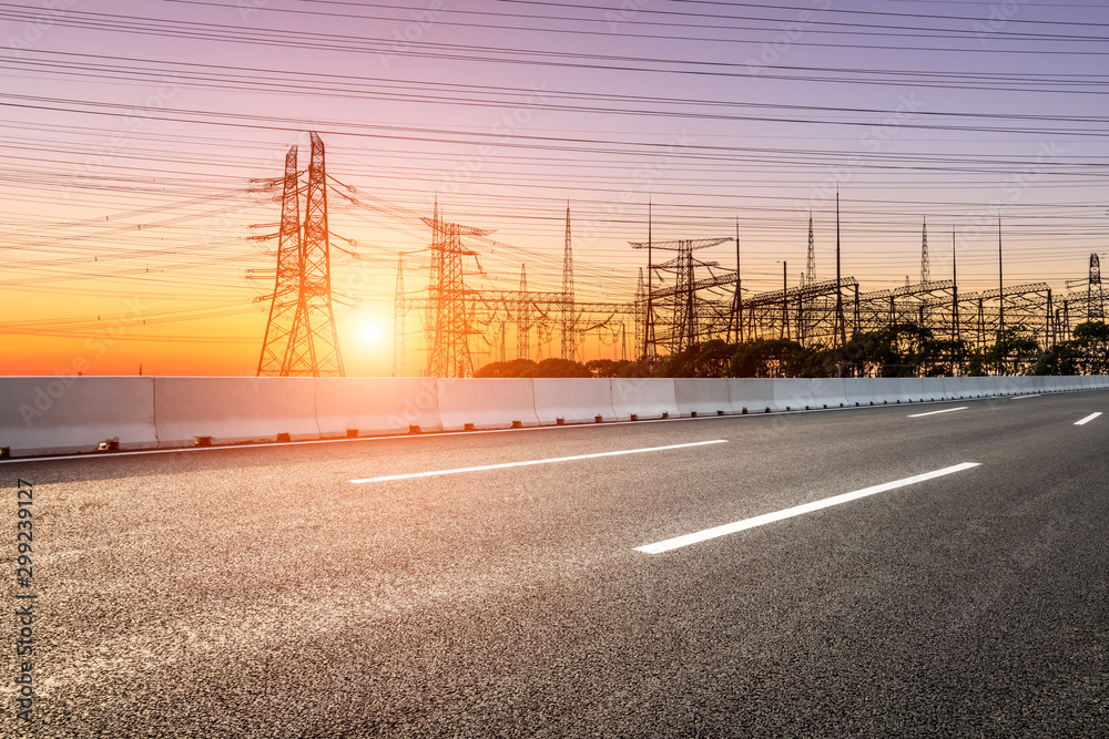 Empty asphalt road and high voltage electricity tower landscape at sunset.