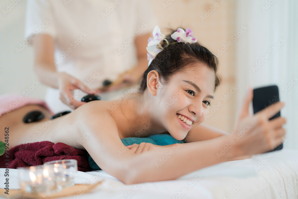 Beautiful young Asian woman smile and holding smartphone receiving rock therapy massage taking selfi