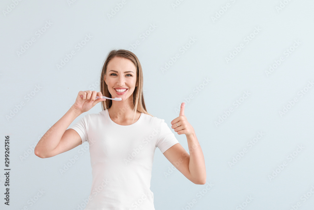 Portrait of woman brushing teeth on light background