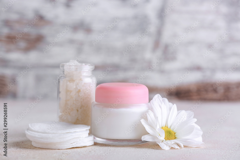 Jar of cosmetics cream with sea salt and cotton sponges on light background