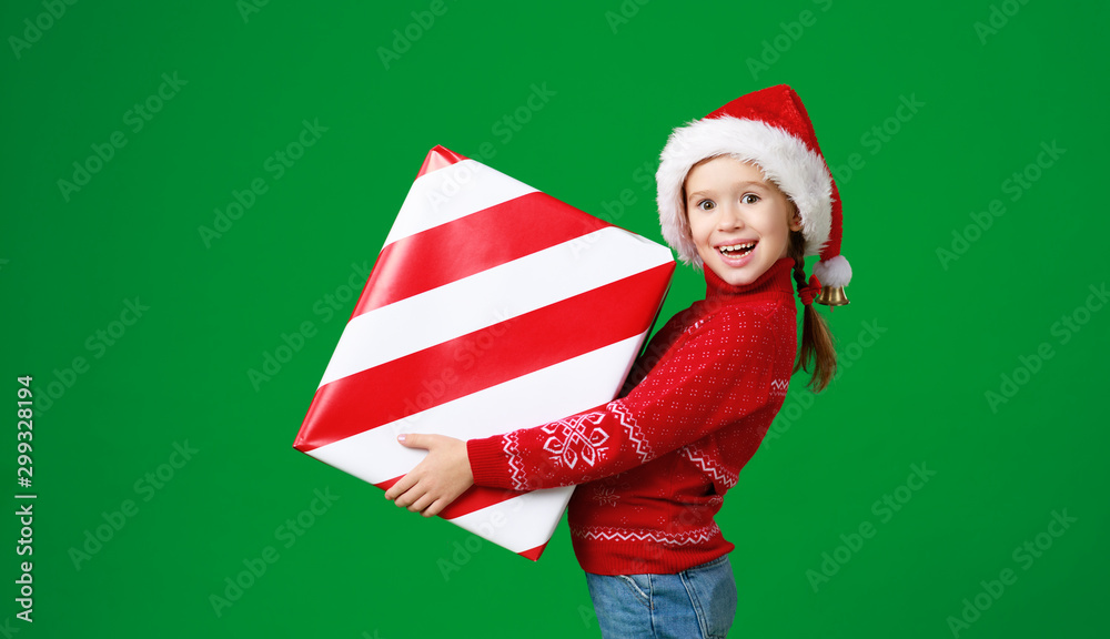 happy funny child girl in red Christmas hat   with gift on green   background.