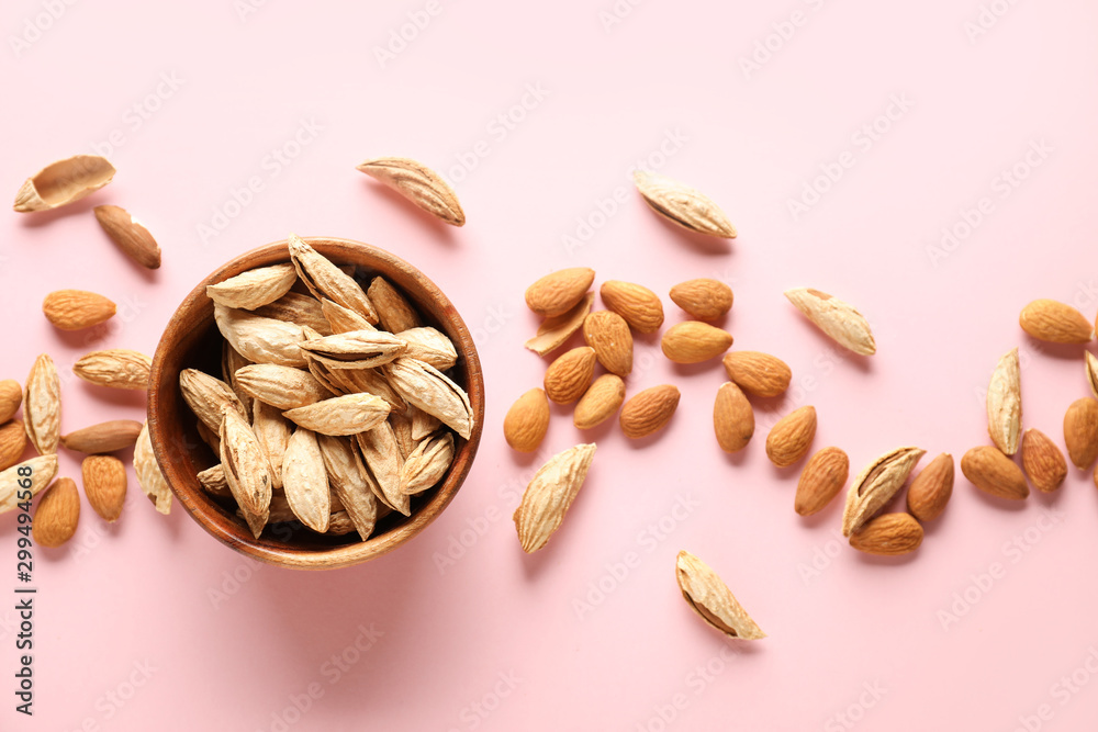 Bowl with tasty almonds on color background