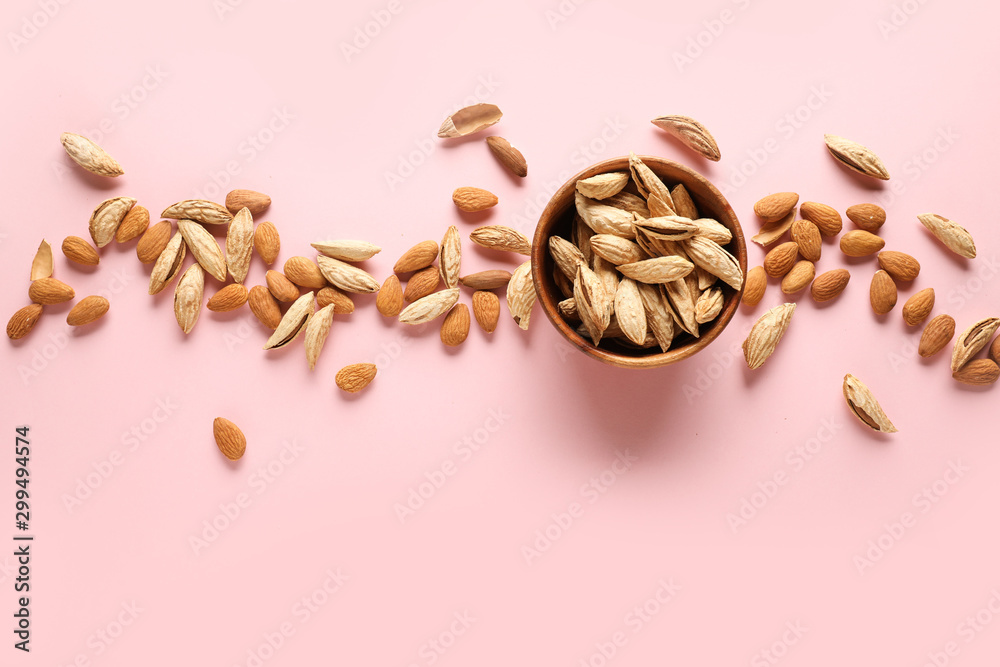 Bowl with tasty almonds on color background