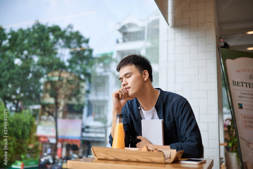 Handsome young freelancer is having a coffee break and dreaming after working at the coffee shop