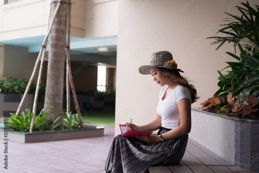 Elegant Asian woman writing a notebook or diary outside.