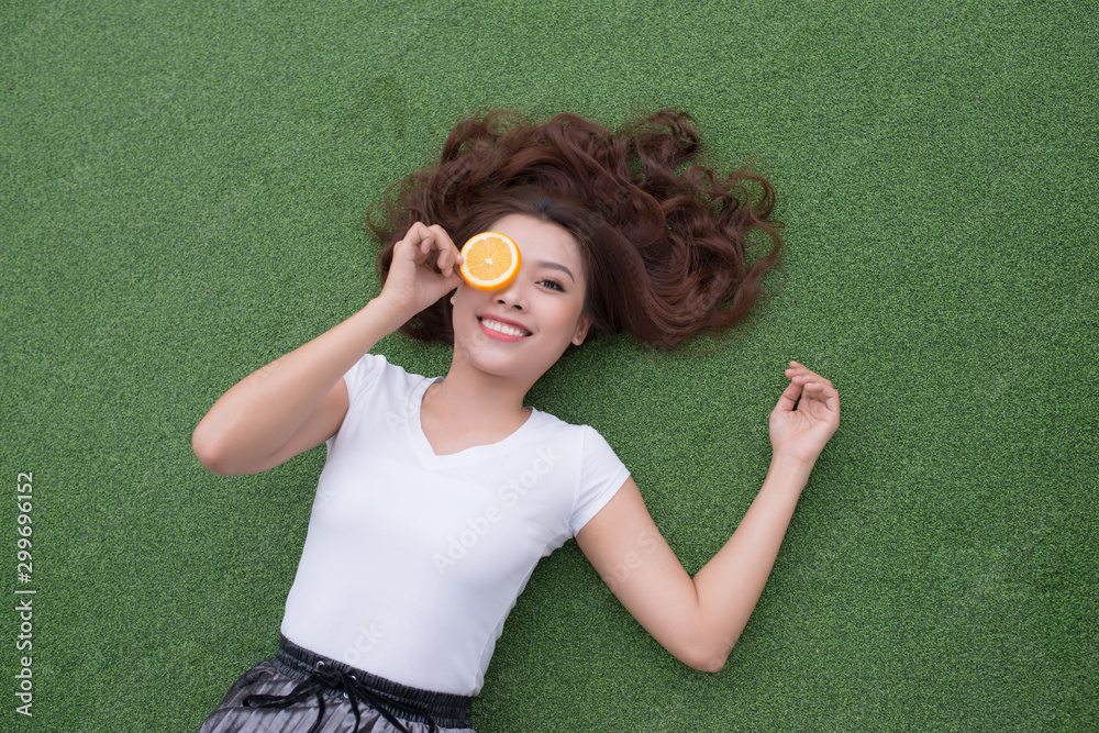 Young Asian woman enjoying the lying on her back on the green grass and hiding her eye with orange p