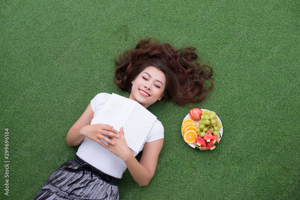 Woman lay down or relaxing on green grass reading book in summer or spring, top view