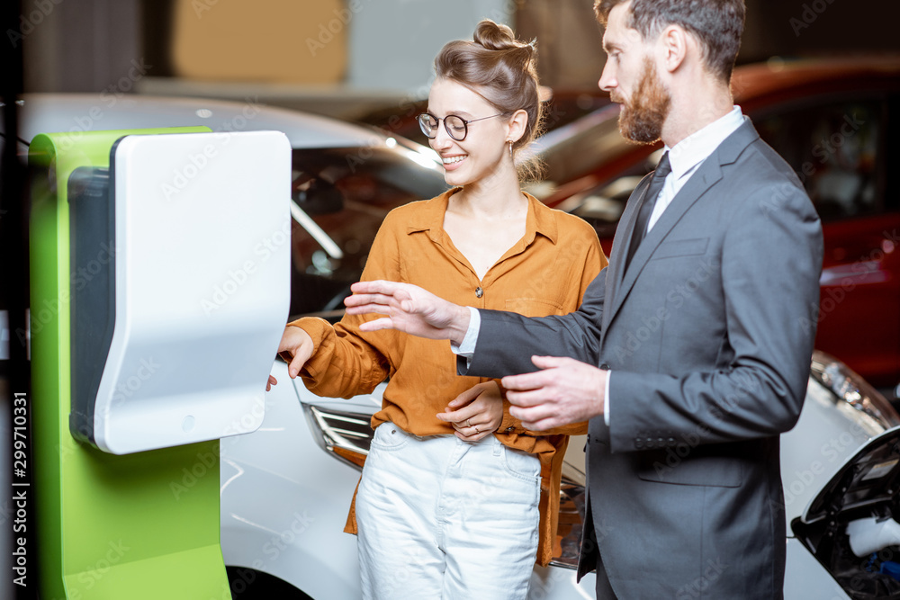 Sales manager with client near the car charging station in the showroom