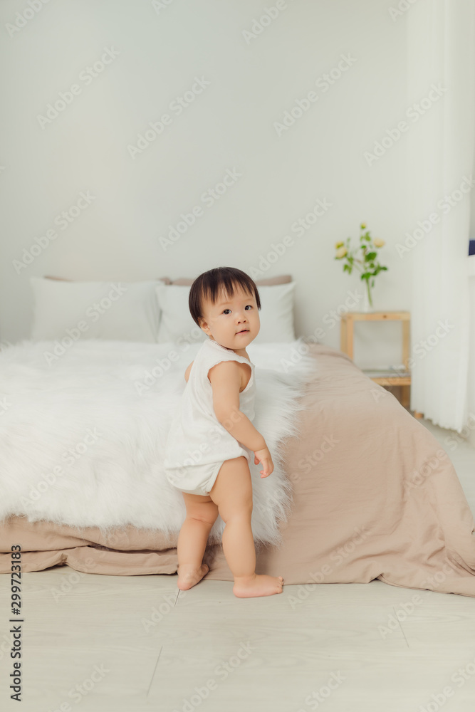 Adorable little girl standing next to the bed at home.