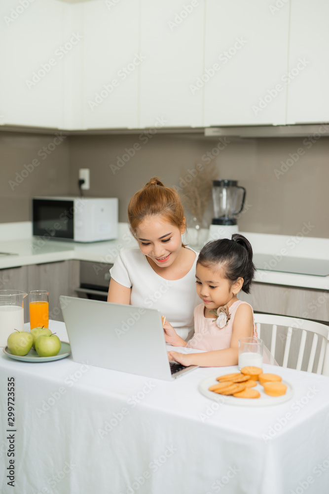 年轻的父母和他们的女儿坐在桌子旁，用笔记本电脑看东西。