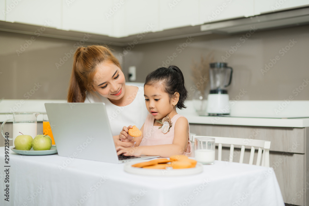 Young parents with they daughter sitting at the table and watching something on laptop.