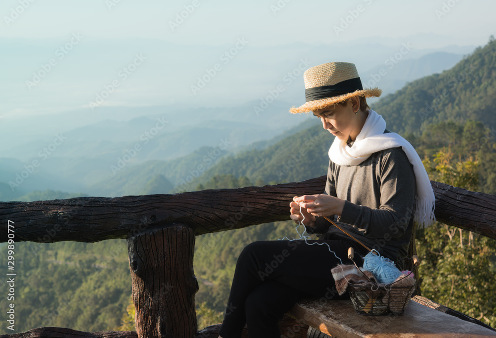 亚洲中年妇女坐在长椅上，在野兽般的自然环境中编织冬季圣诞节