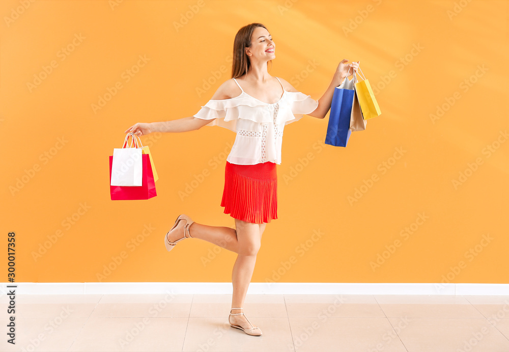 Beautiful young woman with shopping bags near color wall