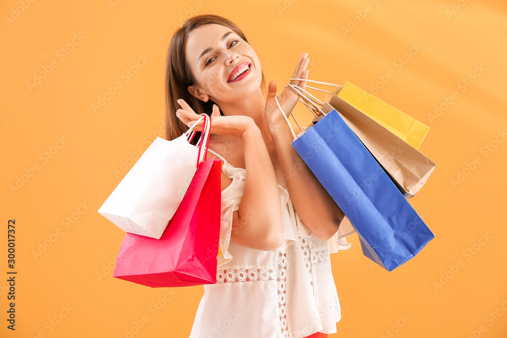 Beautiful young woman with shopping bags on color background