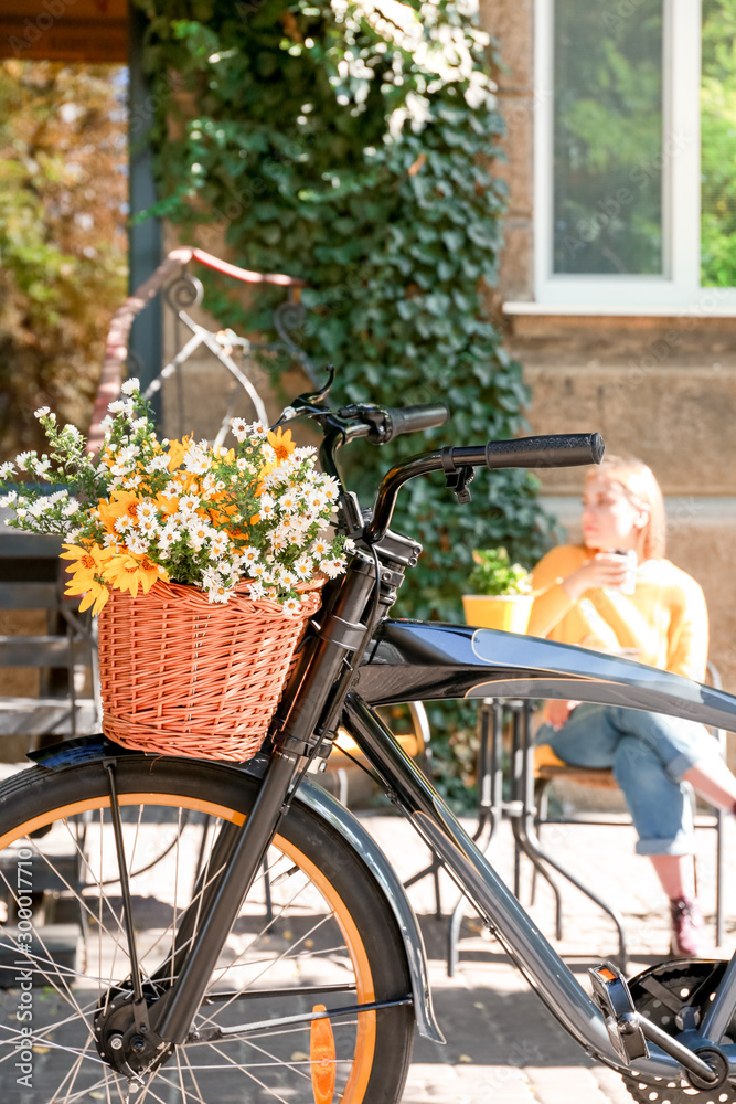 Modern bicycle with basket and bouquet of flowers on city street