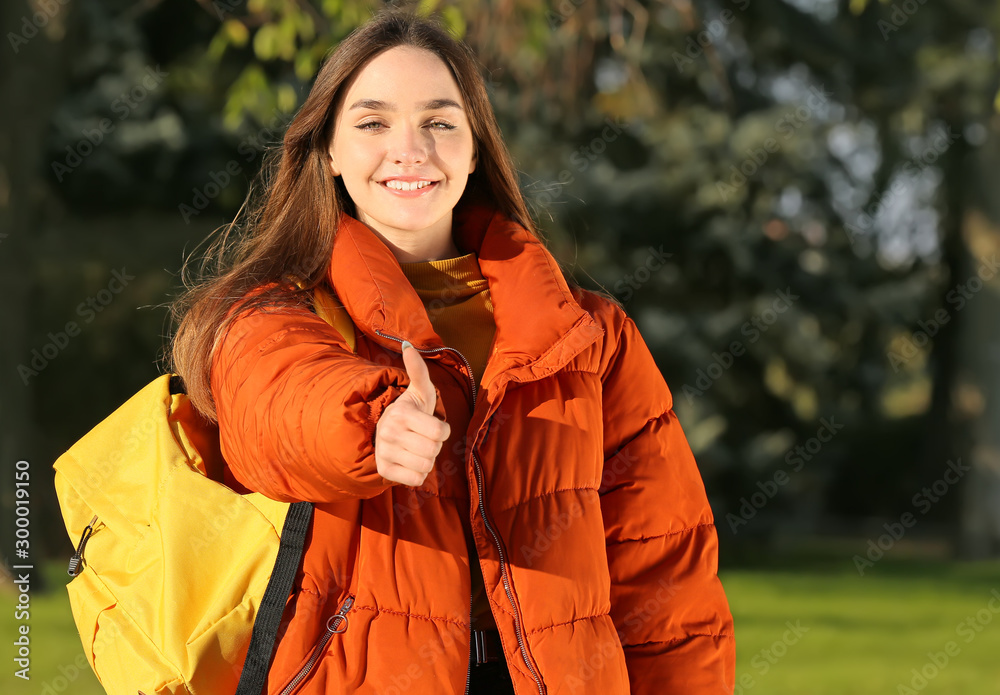 Portrait of teenage female student showing thumb-up outdoors