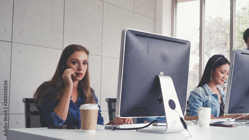 Customer support agent or call center with headset works on desktop computer while supporting the cu