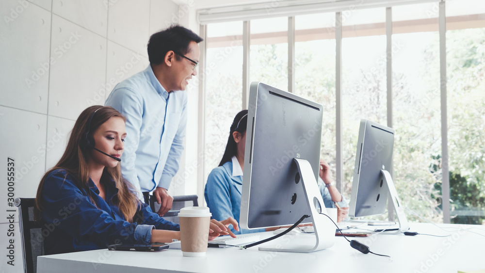 Customer support agent or call center with headset works on desktop computer while supporting the cu