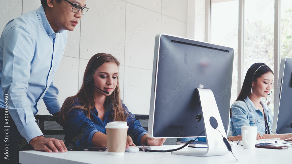 Customer support agent or call center with headset works on desktop computer while supporting the cu