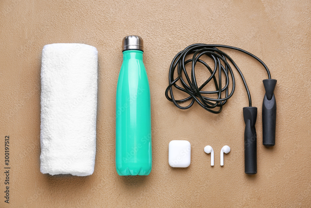 Sports water bottle, towel, jumping rope and earphones on color background