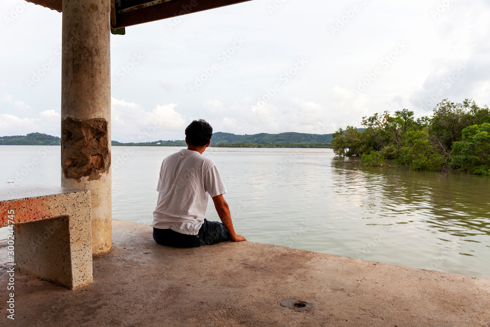 Lonely asian man sitting alone on a pier in bad weather day