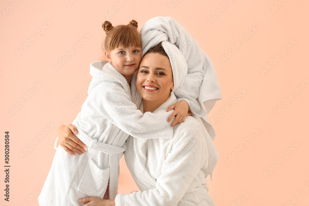 Portrait of happy mother and daughter in bathrobes on color background