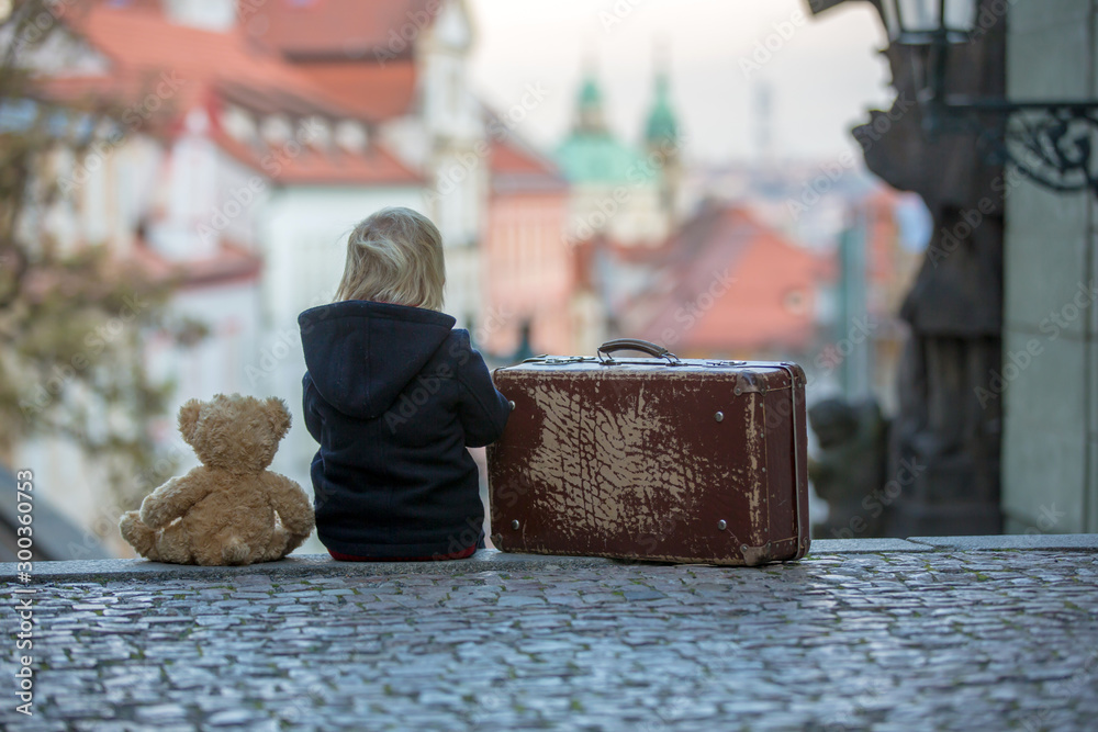 Beautiful child with old vintage suitcase and teddy bear, casually dressed, looking at night view of